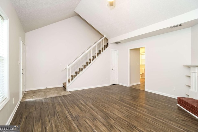 unfurnished living room featuring a textured ceiling, dark hardwood / wood-style flooring, and lofted ceiling