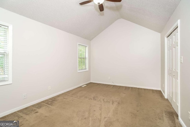 unfurnished bedroom featuring a closet, carpet floors, a textured ceiling, lofted ceiling, and ceiling fan