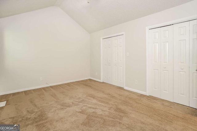 unfurnished bedroom with multiple closets, lofted ceiling, and light colored carpet