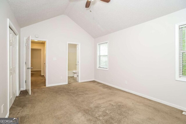 unfurnished bedroom featuring vaulted ceiling, light colored carpet, multiple windows, and ceiling fan