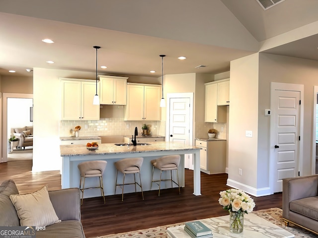 kitchen featuring light stone counters, white cabinets, open floor plan, hanging light fixtures, and an island with sink