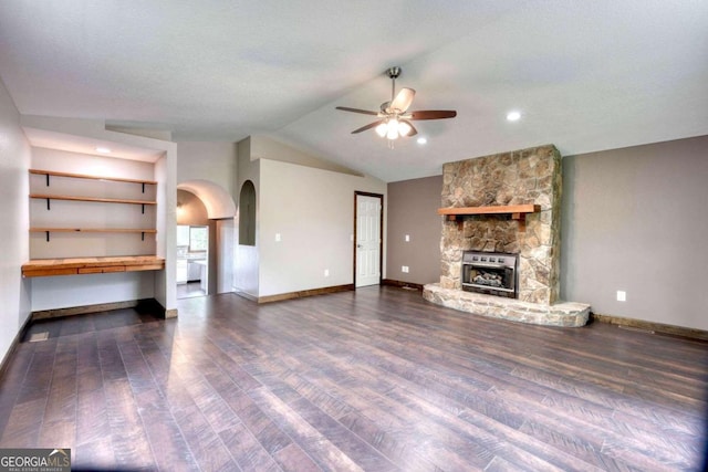 unfurnished living room featuring ceiling fan, lofted ceiling, a stone fireplace, and dark hardwood / wood-style flooring