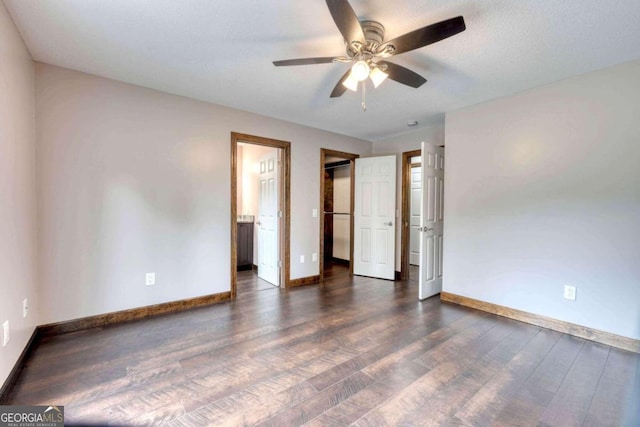 unfurnished bedroom with dark wood-type flooring, ensuite bathroom, a spacious closet, a closet, and ceiling fan