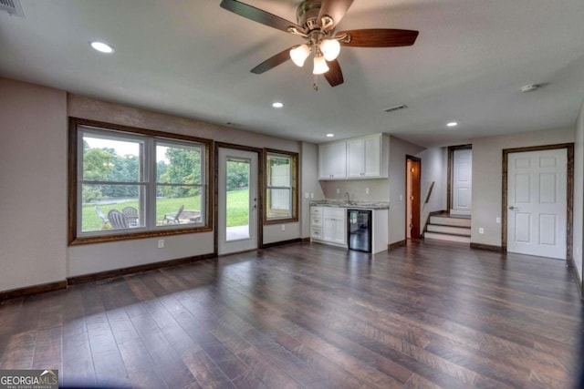 unfurnished living room featuring wine cooler, ceiling fan, dark wood-type flooring, and indoor wet bar