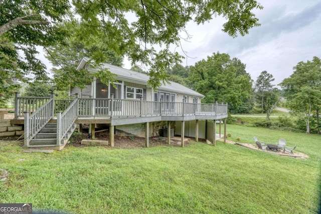 rear view of property featuring a wooden deck, a fire pit, and a lawn