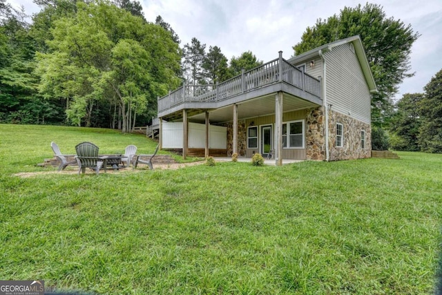 rear view of property featuring a wooden deck, a lawn, and an outdoor fire pit