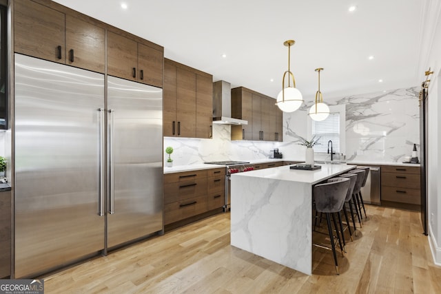 kitchen with light hardwood / wood-style floors, high quality appliances, backsplash, and wall chimney exhaust hood