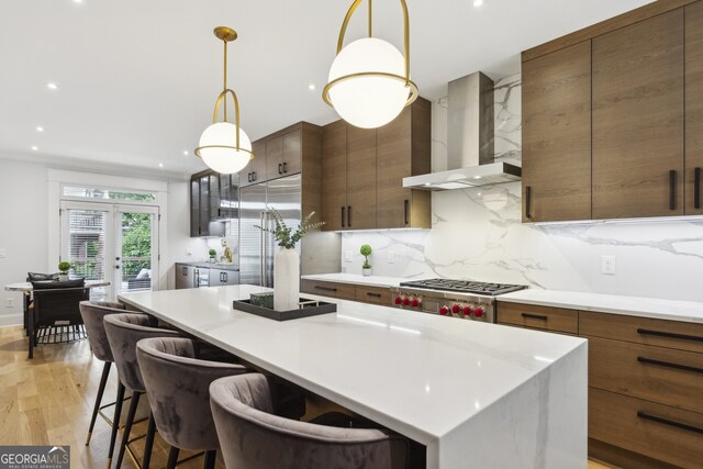 kitchen featuring decorative backsplash, pendant lighting, wall chimney exhaust hood, a center island, and light hardwood / wood-style flooring