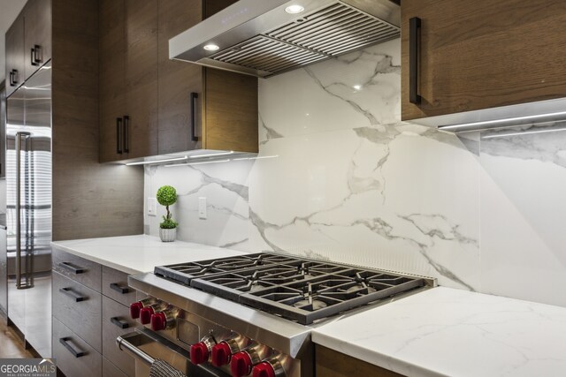 kitchen with high end stainless steel range, dark brown cabinets, tasteful backsplash, premium range hood, and light stone counters