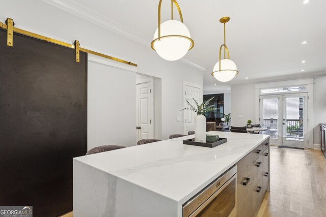 kitchen with crown molding, light wood-type flooring, a kitchen island, a barn door, and light stone countertops