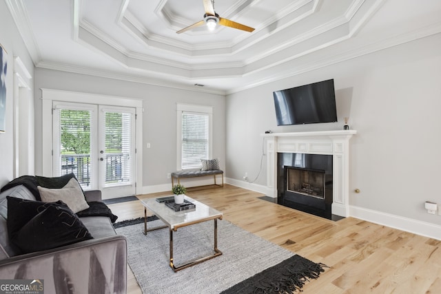 living room featuring ornamental molding, light wood-type flooring, ceiling fan, and a raised ceiling