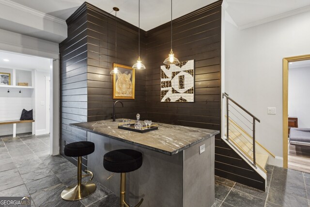 kitchen with a breakfast bar area, dark tile patterned floors, dark stone counters, pendant lighting, and ornamental molding