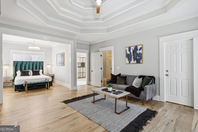 living room with an inviting chandelier, light wood-type flooring, a tray ceiling, and ornamental molding