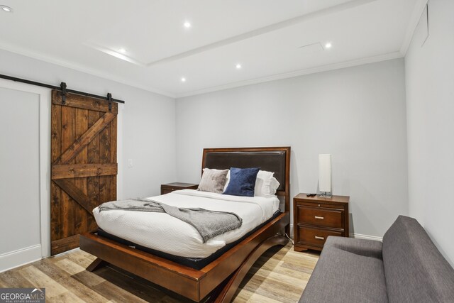 bedroom featuring crown molding, light hardwood / wood-style flooring, and a barn door