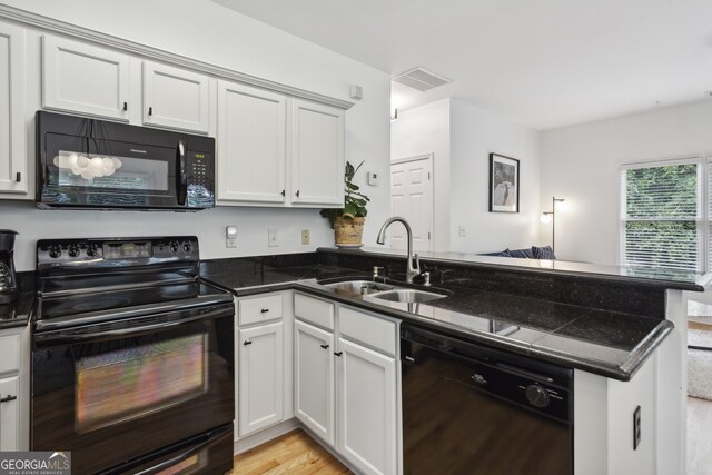 kitchen featuring light hardwood / wood-style flooring, black appliances, dark stone counters, sink, and kitchen peninsula