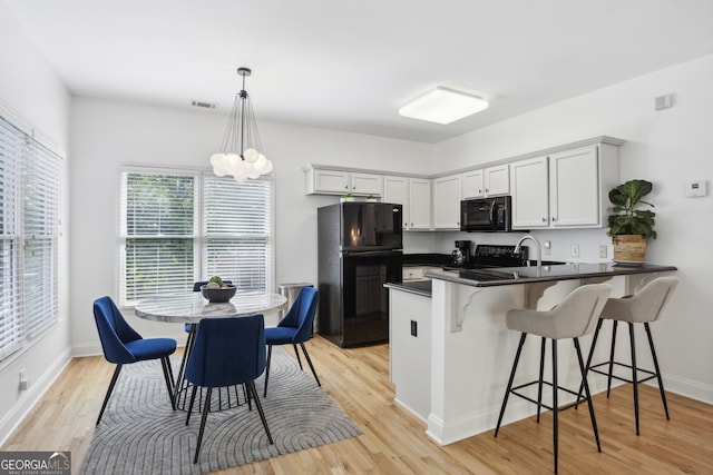 kitchen with black appliances, hanging light fixtures, light hardwood / wood-style flooring, kitchen peninsula, and a kitchen breakfast bar