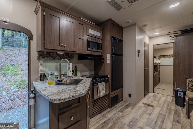 kitchen with stainless steel microwave, light hardwood / wood-style flooring, dark brown cabinets, black range, and sink