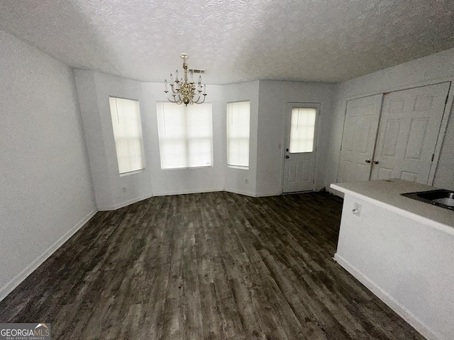 unfurnished dining area featuring dark wood-type flooring, a textured ceiling, and a chandelier