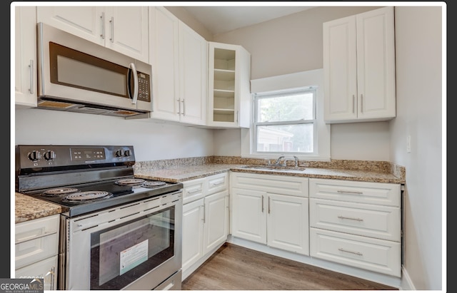 kitchen with white cabinets, sink, light stone countertops, range with electric cooktop, and light hardwood / wood-style floors