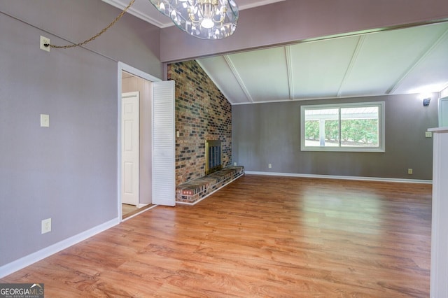 unfurnished living room featuring a brick fireplace, crown molding, an inviting chandelier, light hardwood / wood-style flooring, and lofted ceiling