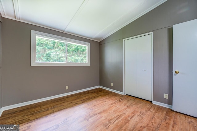 unfurnished bedroom with crown molding, a closet, light hardwood / wood-style floors, and vaulted ceiling