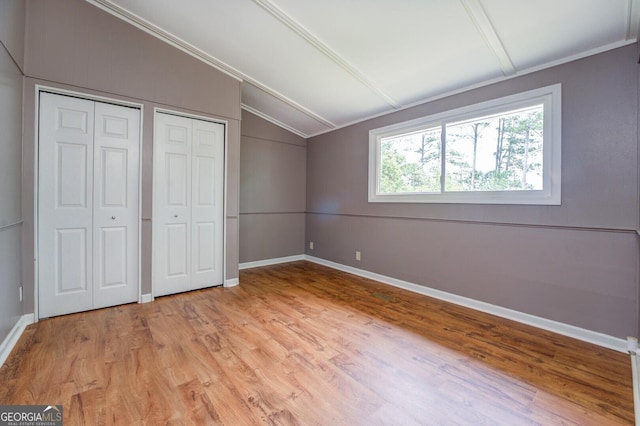 unfurnished bedroom with two closets, ornamental molding, light hardwood / wood-style flooring, and vaulted ceiling