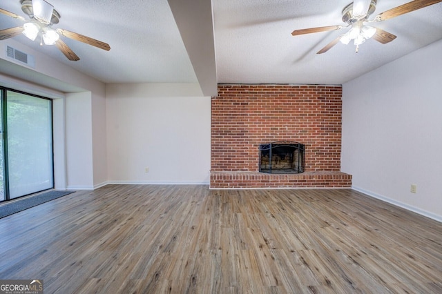 unfurnished living room with a fireplace, ceiling fan, light wood-type flooring, and a textured ceiling