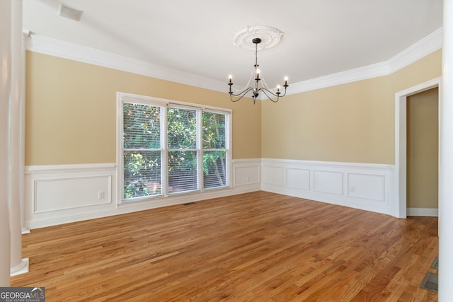 empty room featuring a chandelier, wainscoting, ornamental molding, and light wood finished floors