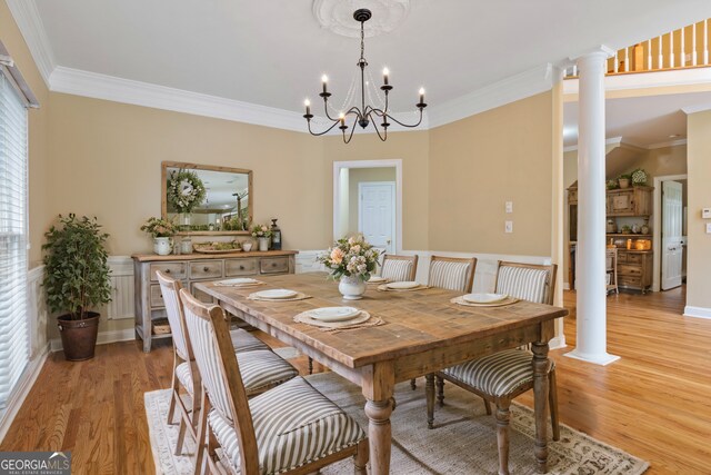 dining room with light hardwood / wood-style floors, ornamental molding, an inviting chandelier, and decorative columns