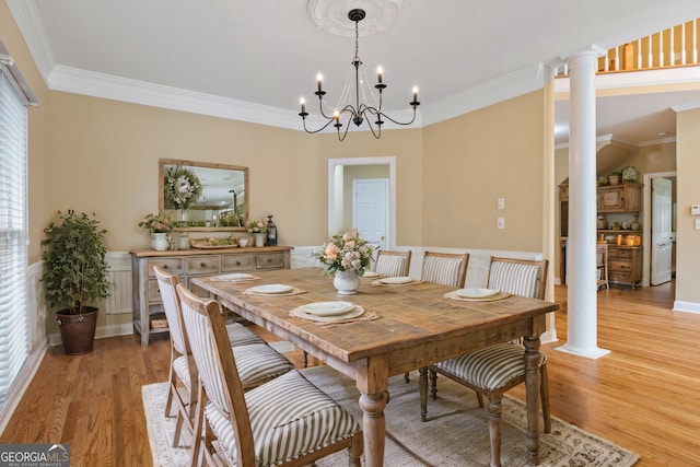 dining area with light wood-style floors, a chandelier, crown molding, and ornate columns