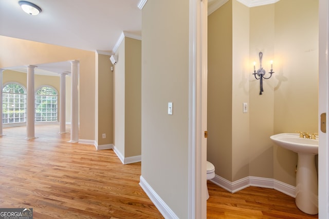 bathroom with toilet, wood finished floors, baseboards, ornate columns, and crown molding