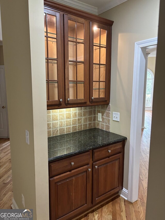 bar with light hardwood / wood-style floors, dark stone counters, ornamental molding, and decorative backsplash