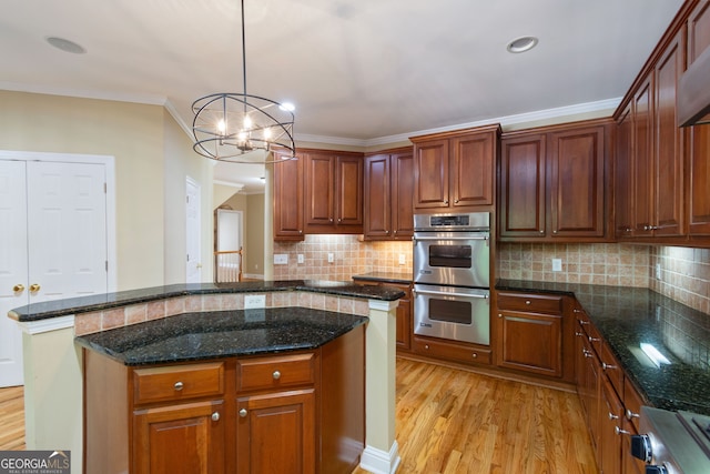 kitchen with double oven, ornamental molding, light wood-type flooring, backsplash, and decorative light fixtures