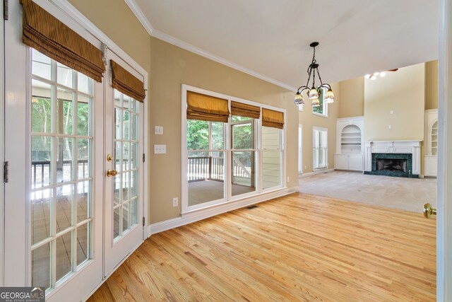 unfurnished living room with a premium fireplace, french doors, crown molding, light wood-type flooring, and a chandelier