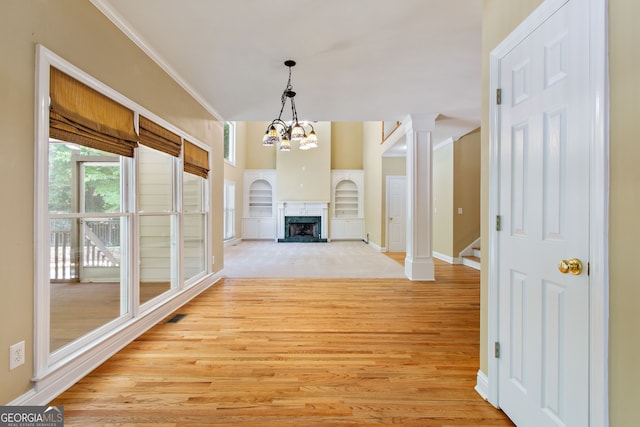 unfurnished living room with light wood-style flooring, a premium fireplace, ornate columns, an inviting chandelier, and crown molding