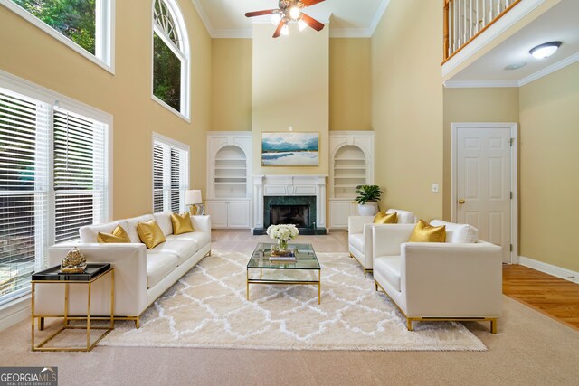 living room with light wood-type flooring, a high ceiling, ceiling fan, a premium fireplace, and ornamental molding