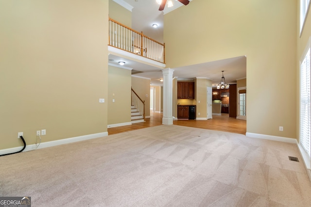 unfurnished living room with crown molding, baseboards, light carpet, ornate columns, and stairs