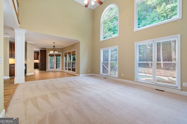 unfurnished living room with light carpet, decorative columns, visible vents, and ceiling fan with notable chandelier