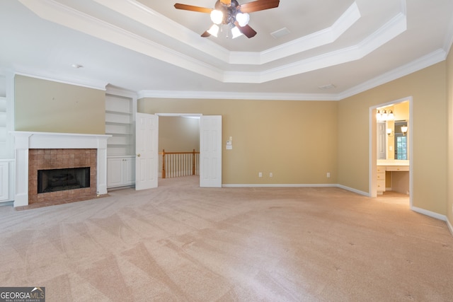 unfurnished living room featuring ornamental molding, a tray ceiling, a tiled fireplace, and light colored carpet