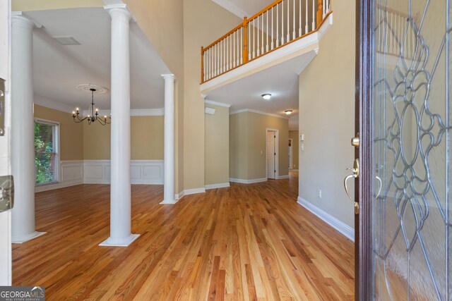 foyer with ornate columns, ornamental molding, light wood-type flooring, and an inviting chandelier