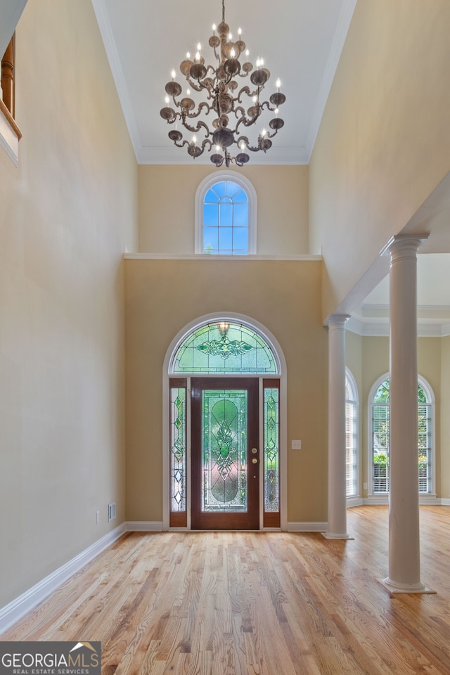 foyer with baseboards, a towering ceiling, wood finished floors, crown molding, and ornate columns