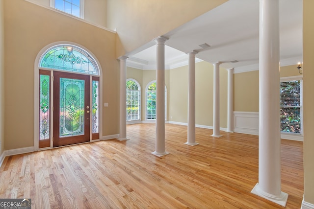 entrance foyer featuring decorative columns, visible vents, a towering ceiling, ornamental molding, and wood finished floors