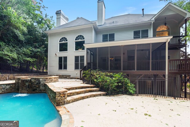 rear view of house with a balcony, pool water feature, a swimming pool with hot tub, a sunroom, and a patio