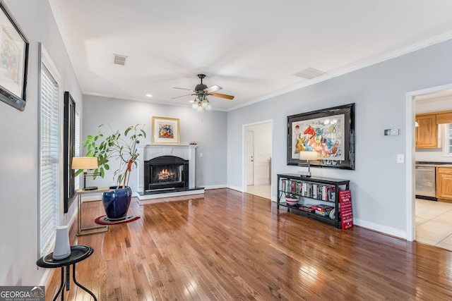 living room with a warm lit fireplace, visible vents, light wood-style floors, baseboards, and crown molding