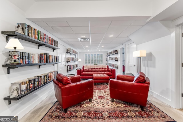 living area featuring a paneled ceiling, wood finished floors, visible vents, and baseboards