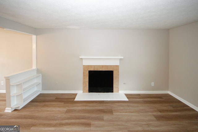 unfurnished living room with hardwood / wood-style flooring, a textured ceiling, and a tile fireplace