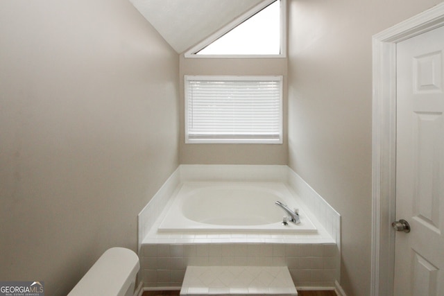 bathroom featuring tiled tub, toilet, and vaulted ceiling