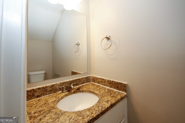 bathroom featuring vanity, toilet, and vaulted ceiling