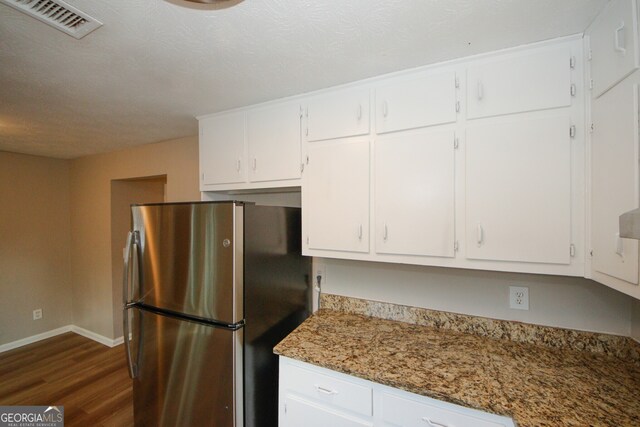 kitchen featuring stainless steel refrigerator, dark stone countertops, dark hardwood / wood-style floors, and white cabinets