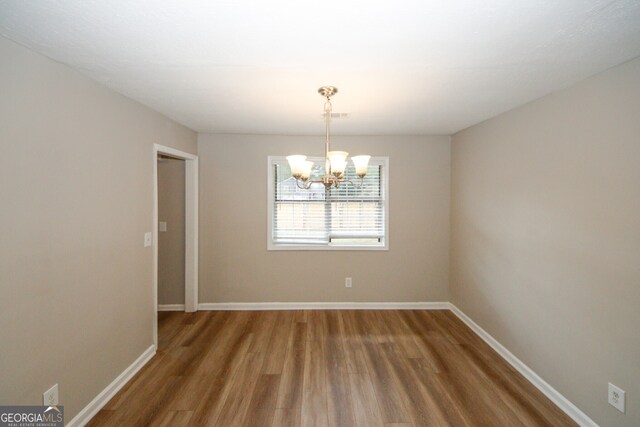 spare room with an inviting chandelier and hardwood / wood-style flooring